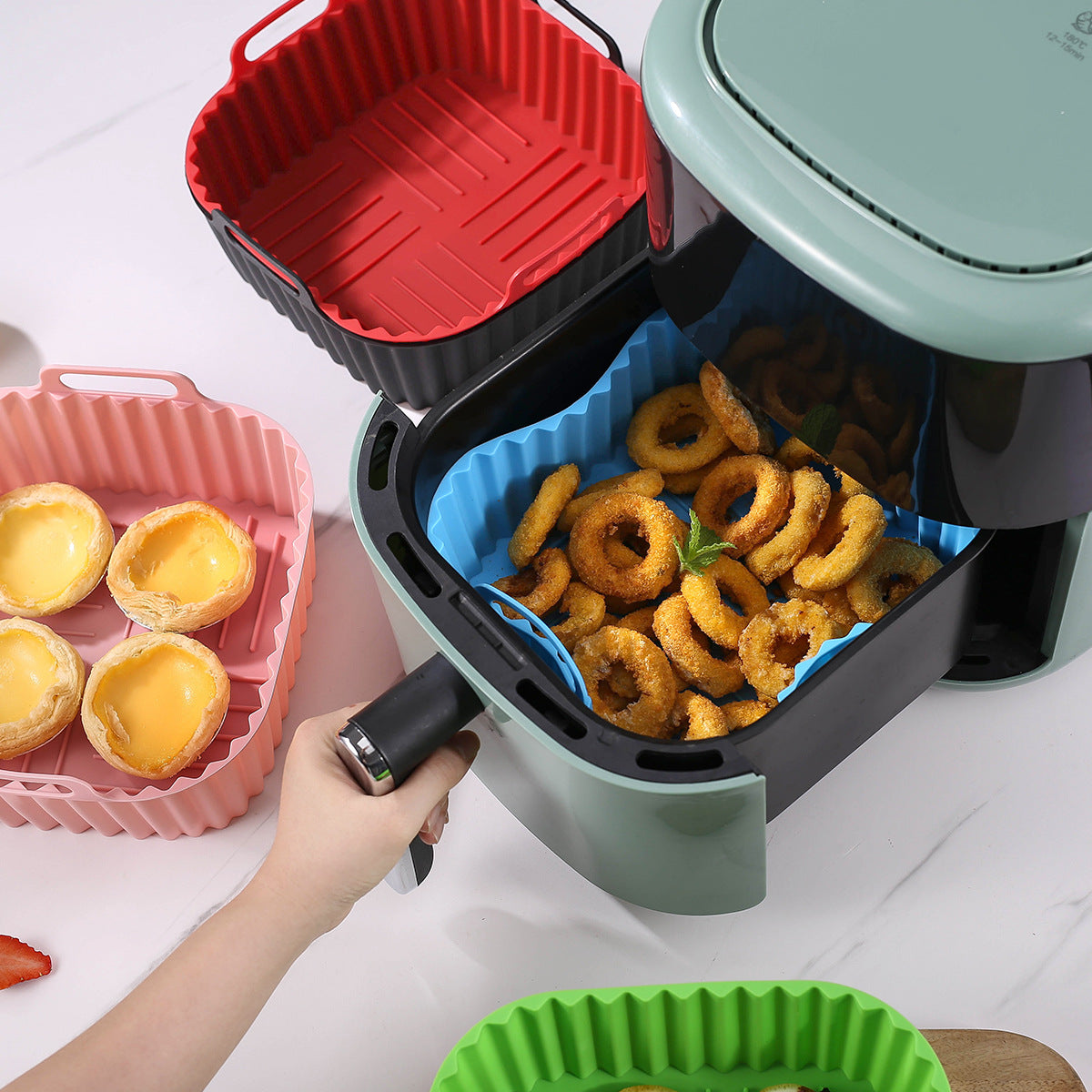 Air fryer trays in different colors with food inside.