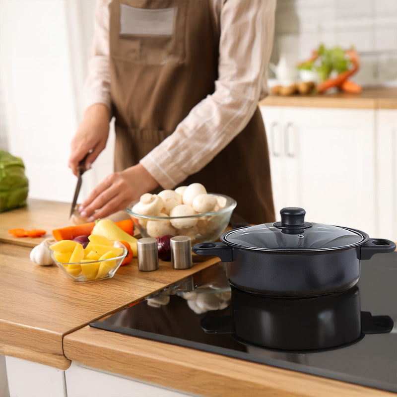 Black casserole on a stove and a woman cutting vegetables.